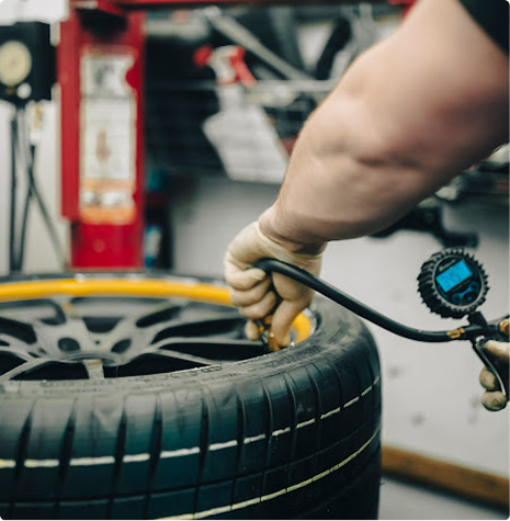 Hand using a tire pressure gauge on a car tire in a garage | Hangar Unlimited Auto Care & Tires