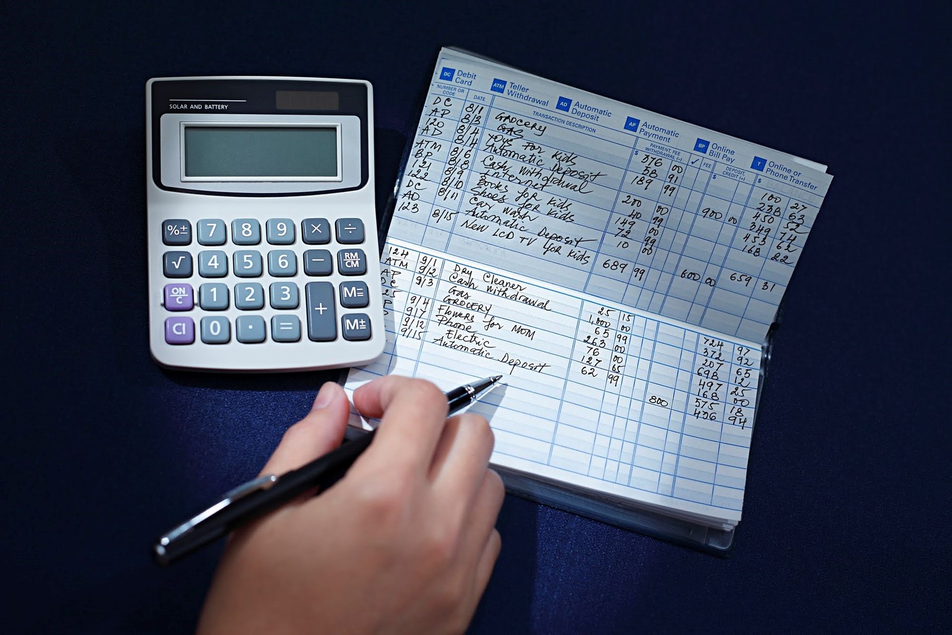 A person is writing in a notebook next to a calculator