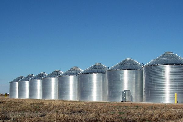 A row of metal silos in a field with a blue sky in the background