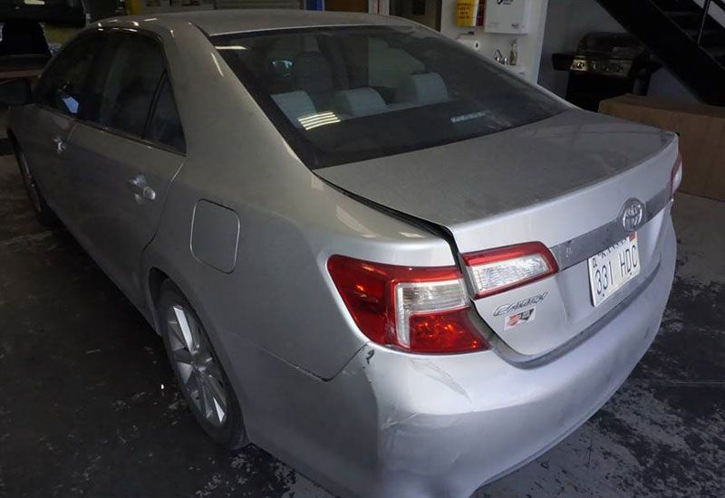 A silver car with a damaged trunk is parked in a garage.