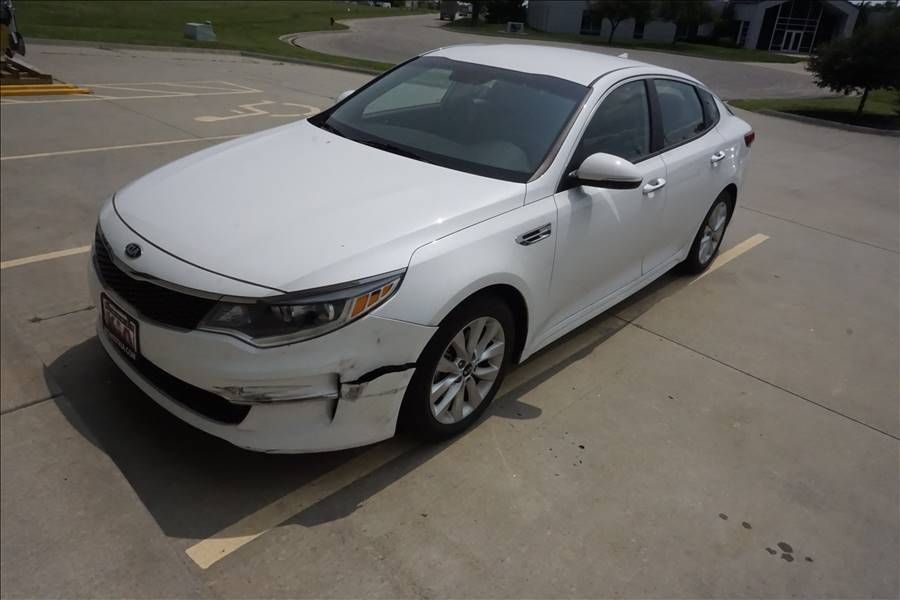 A white car with a damaged front bumper is parked in a parking lot.