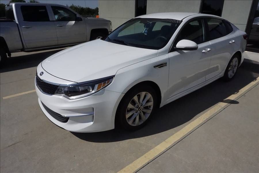 A white car is parked in a parking lot next to a truck.