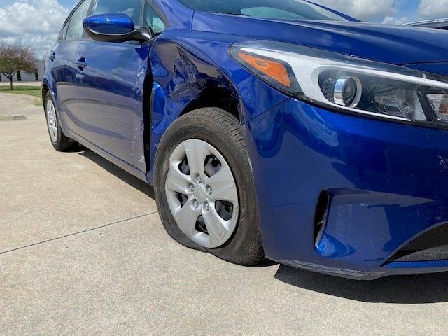 A blue car with a flat tire is parked on the side of the road.