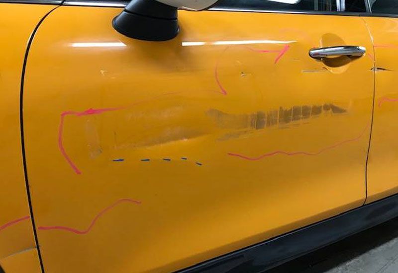 A close up of a yellow car door with scratches on it.
