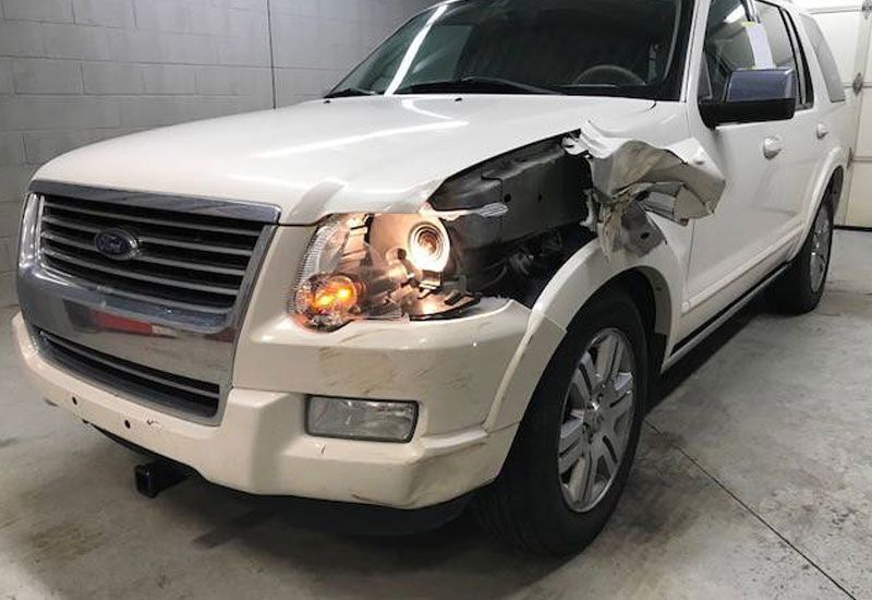 A white ford explorer with a damaged headlight is parked in a garage.