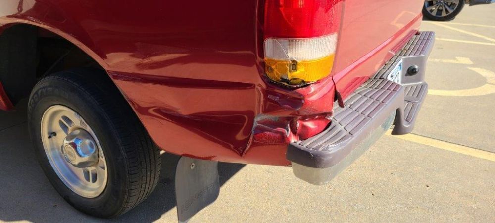 A red truck with a damaged bumper is parked in a parking lot.