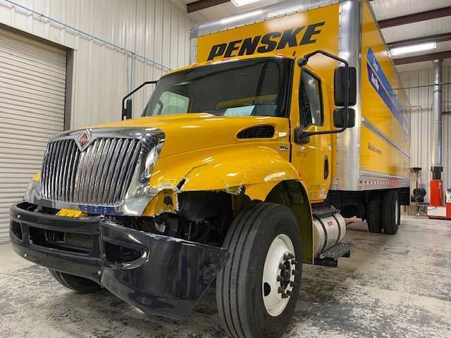 A yellow truck with a bumper missing is parked in a garage.