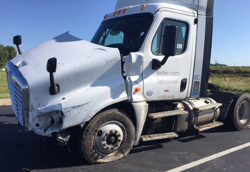 A white semi truck with a broken hood is parked on the side of the road.