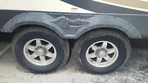 A trailer with a damaged fender and tires is parked in a garage.