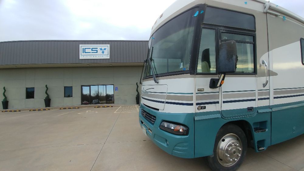 A green and white rv is parked in front of a building.
