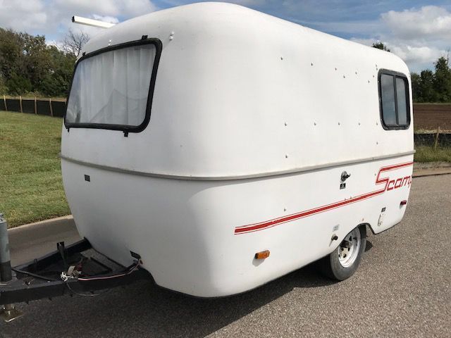 A small white trailer with a red stripe on the side is parked on the side of the road