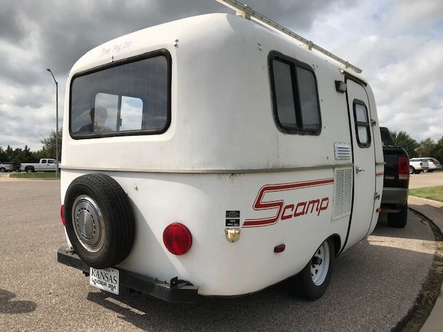 A white scamp trailer is parked in a parking lot