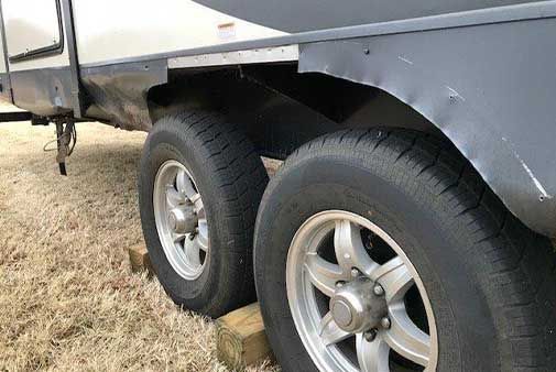 The tires of a trailer are sitting on a wooden block.