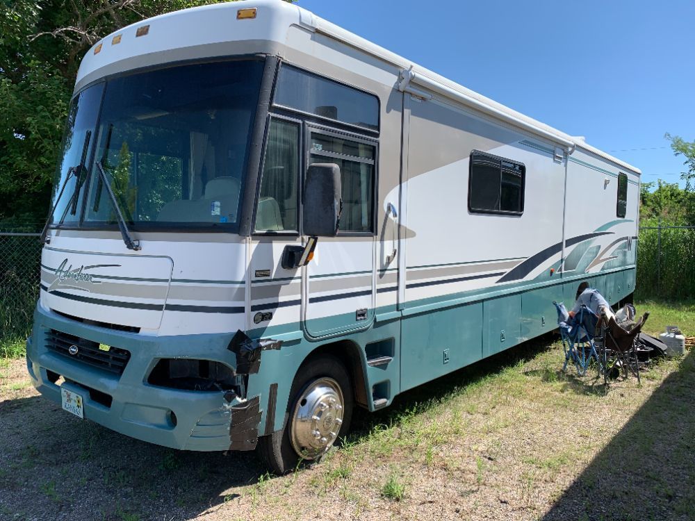 A large white and green rv is parked in a gravel lot.