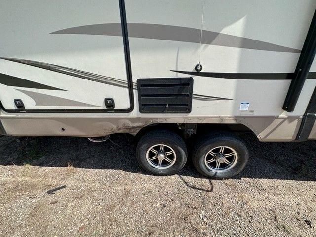 A trailer with two tires is parked on a gravel road.
