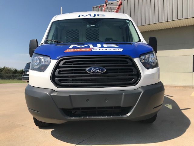 A blue and white ford van is parked in front of a building