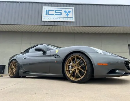 Gray Ferrari sports car with bronze wheels parked outside a collision center.