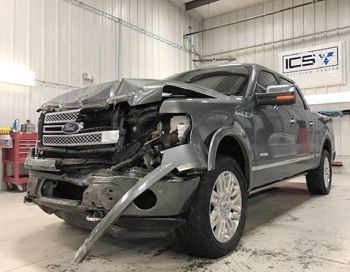 A damaged ford f150 truck is parked in a garage.