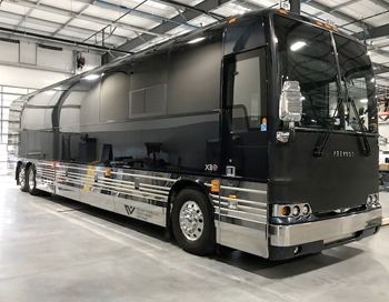 A large black and silver bus is parked in a garage.