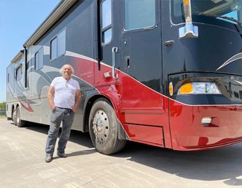 A man is standing in front of a large red and black rv.