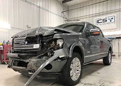 A ford f150 truck with a damaged front end is parked in a garage.