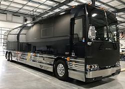 A large black and silver bus is parked in a garage.