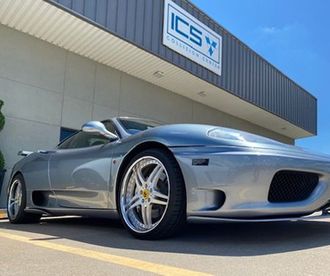 A silver sports car is parked in front of a building that says ics