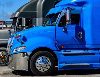 A blue semi truck is parked next to a black semi truck in a parking lot.