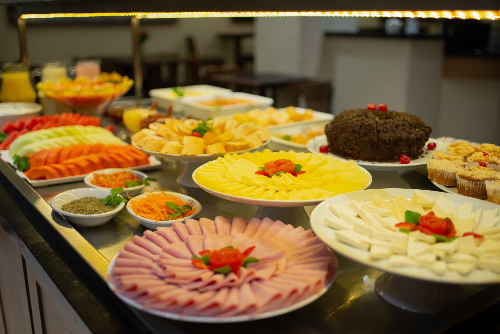 Buffet de café da manhã com frutas fatiadas, queijos, frios e doces.