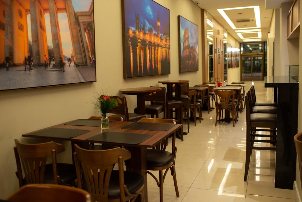 Interior do café com mesas e cadeiras, obras de arte nas paredes e uma área de bar.