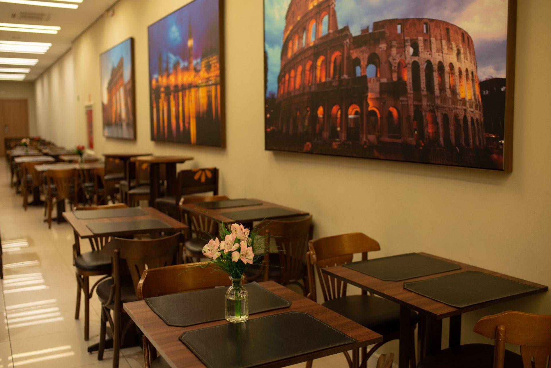 Interior do restaurante com mesas, cadeiras e arte paisagística de uma cidade italiana na parede.