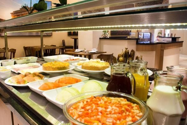 Mesa de bufê com diversos itens alimentares, como bolos, frutas, sucos e tomates em cubos.