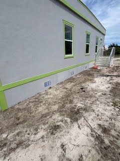 A gray house with green trim is sitting on top of a dirt field.