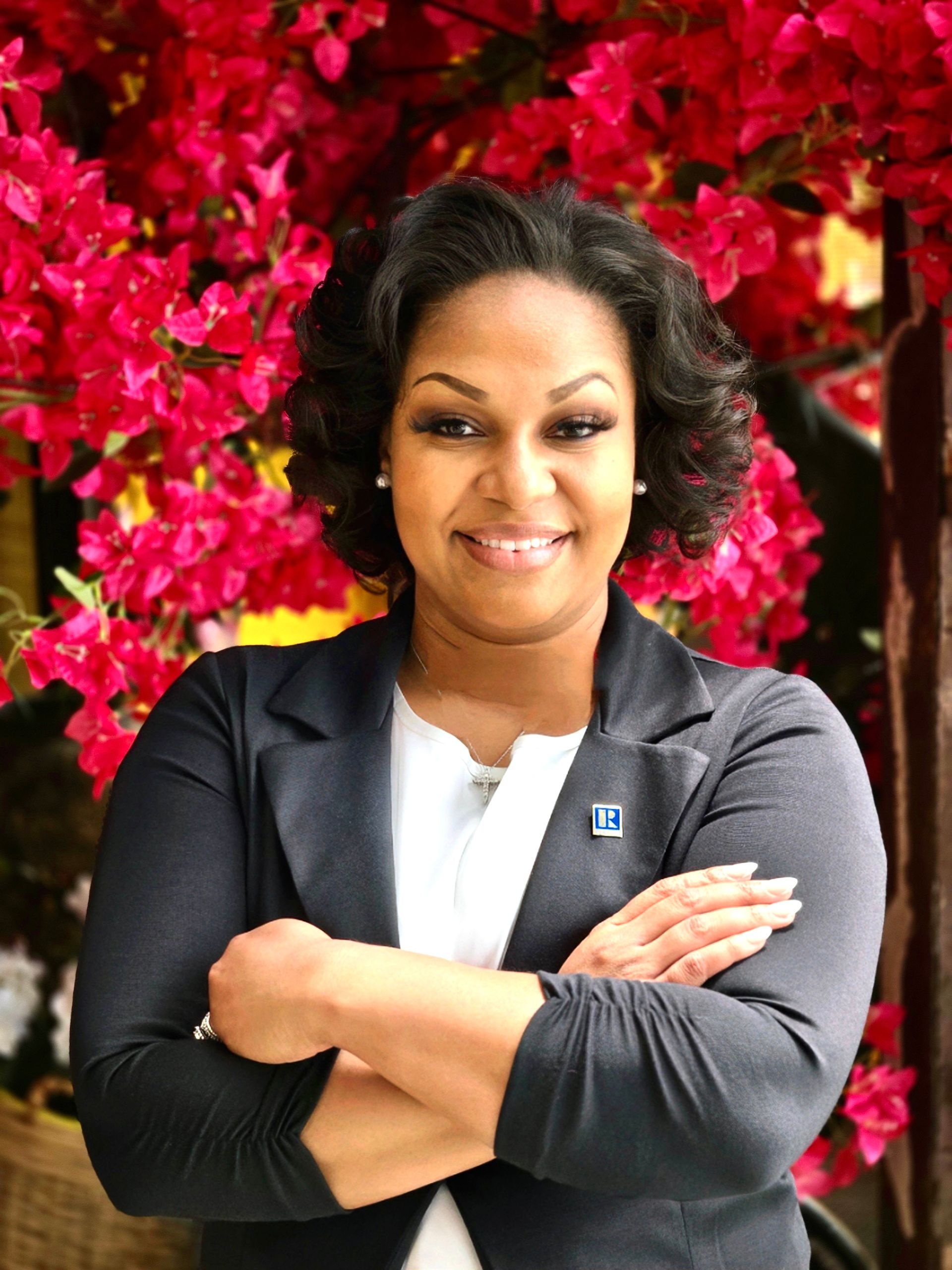 A woman is sitting at a desk with a laptop and a vase of flowers.
