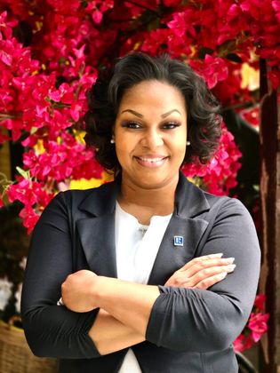 A woman is sitting at a desk with a laptop and a vase of flowers.
