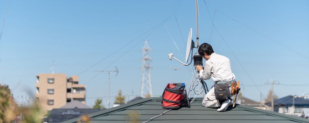 A Man is Kneeling on Top of a Roof Working on a Satellite Dish — Hendo's TV Antennas & Installations in White Rock, QLD