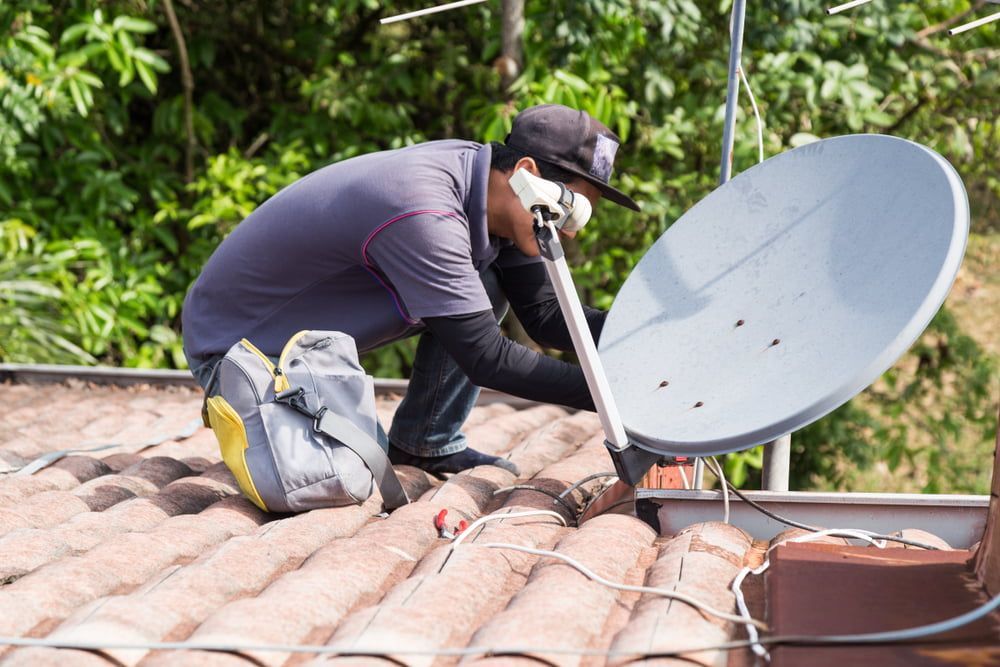 A Man is Working on a Satellite Dish on a Roof — Hendo's TV Antennas & Installations in White Rock, QLD