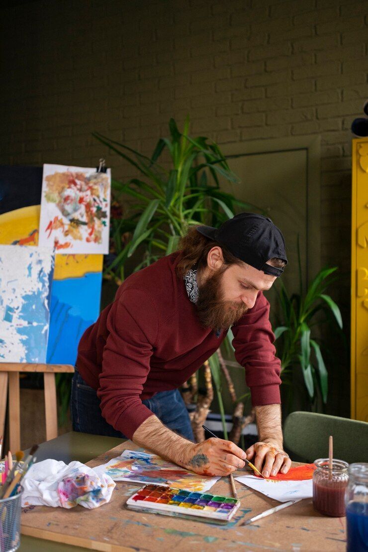 A man is sitting at a table painting with watercolors.