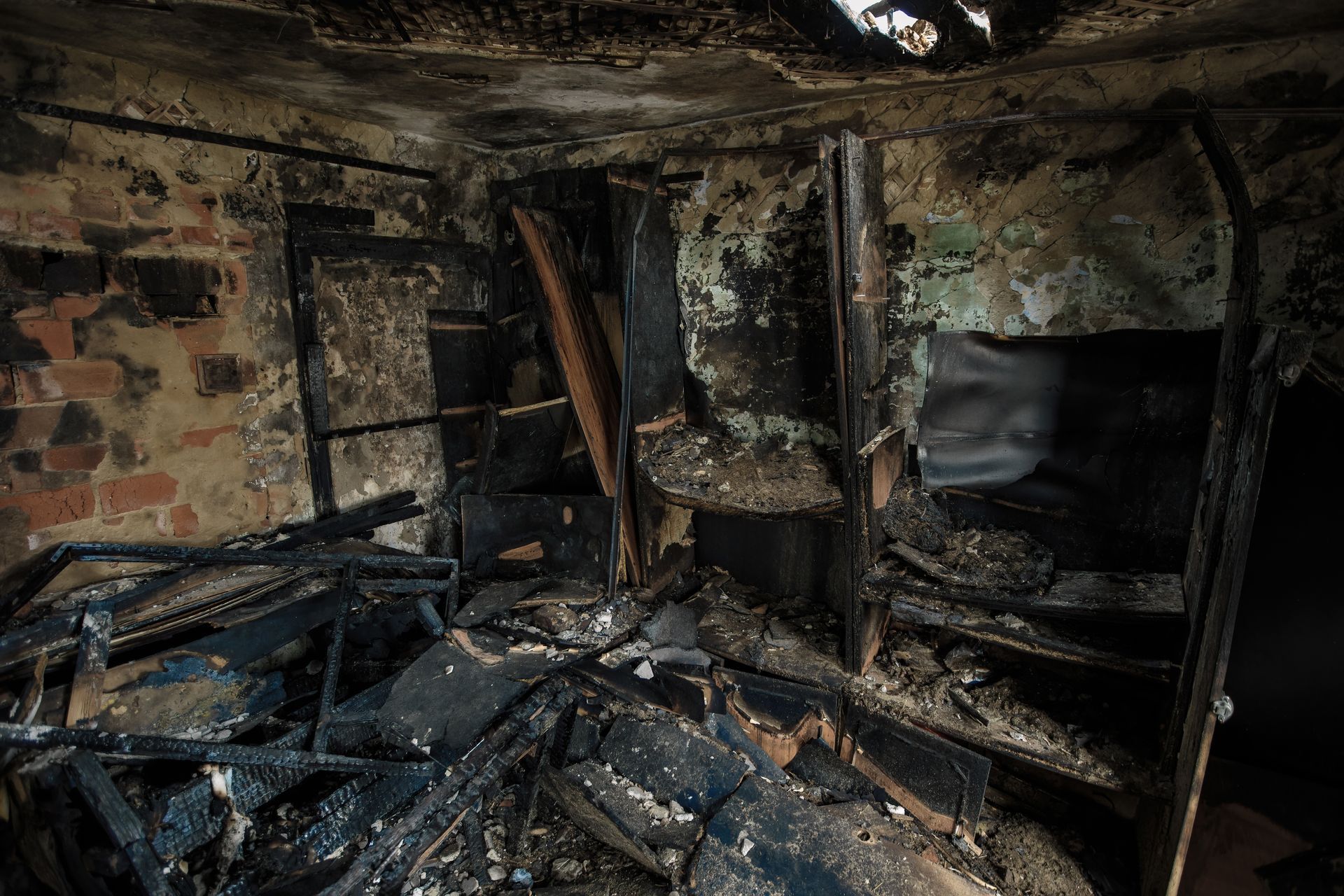 Charred interior of a room after a fire, burnt furniture and debris scattered.