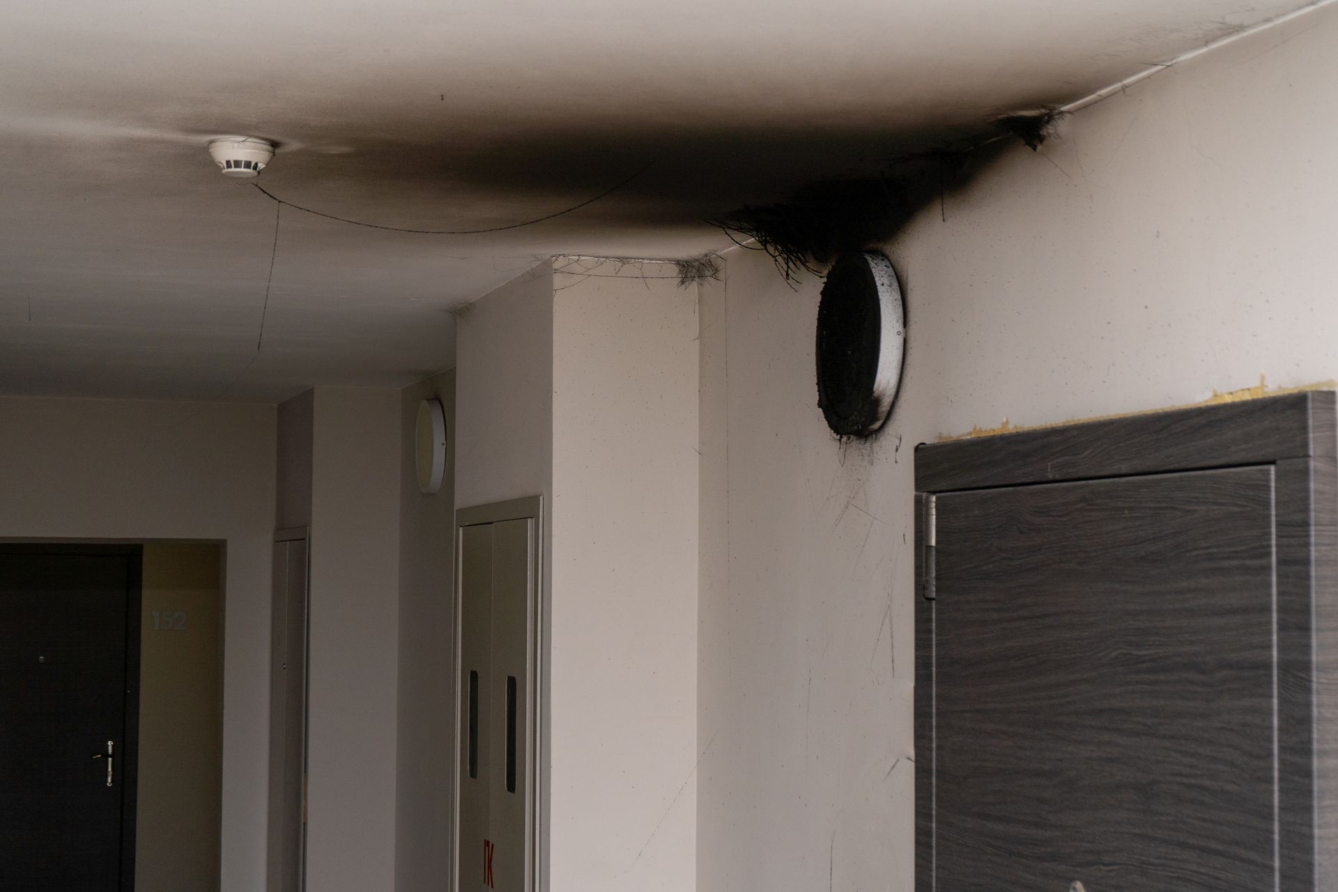 Ceiling and wall with smoke damage around a vent, smoke detector, and door.
