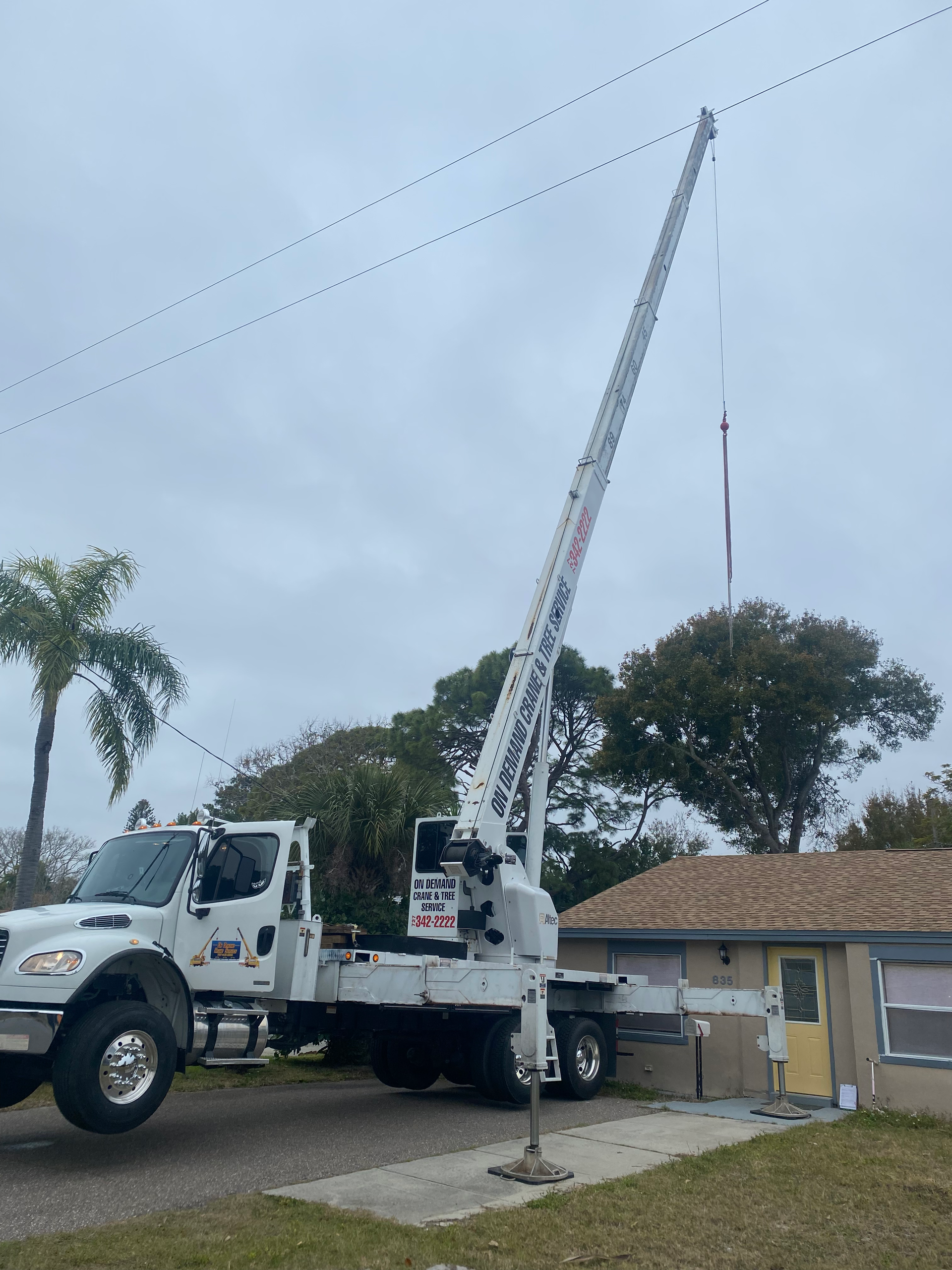 White utility truck with extended boom working near power lines and a small building.