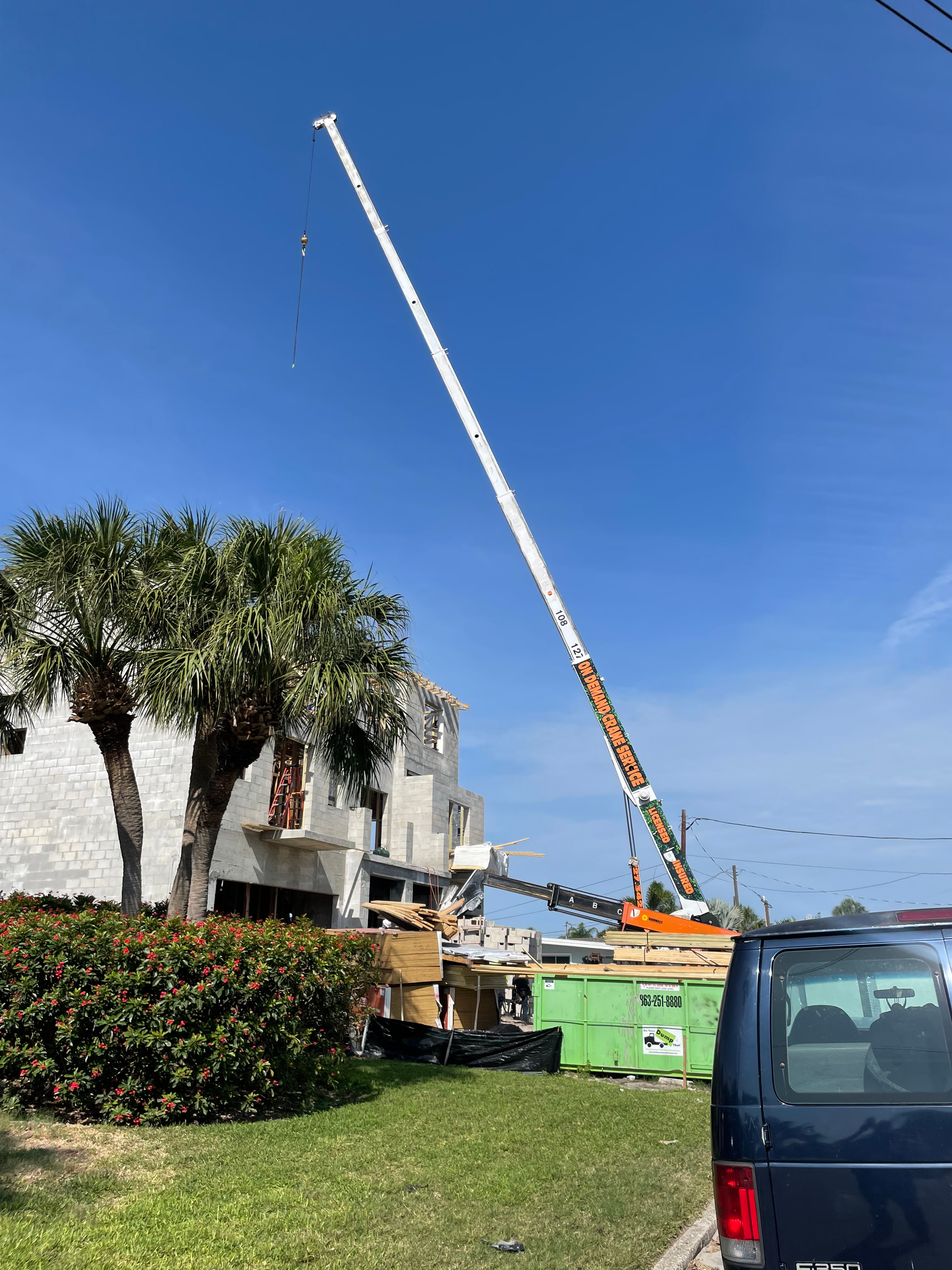 A tall crane next to a building and a blue van parked on a grassy area.