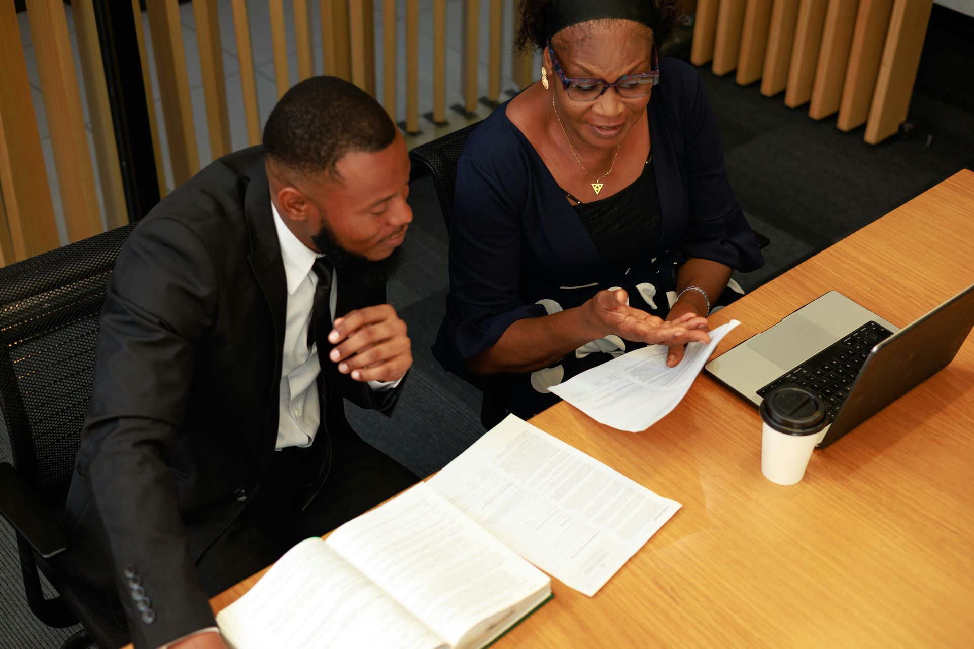 A man and a woman are sitting at a table with a laptop and a book.