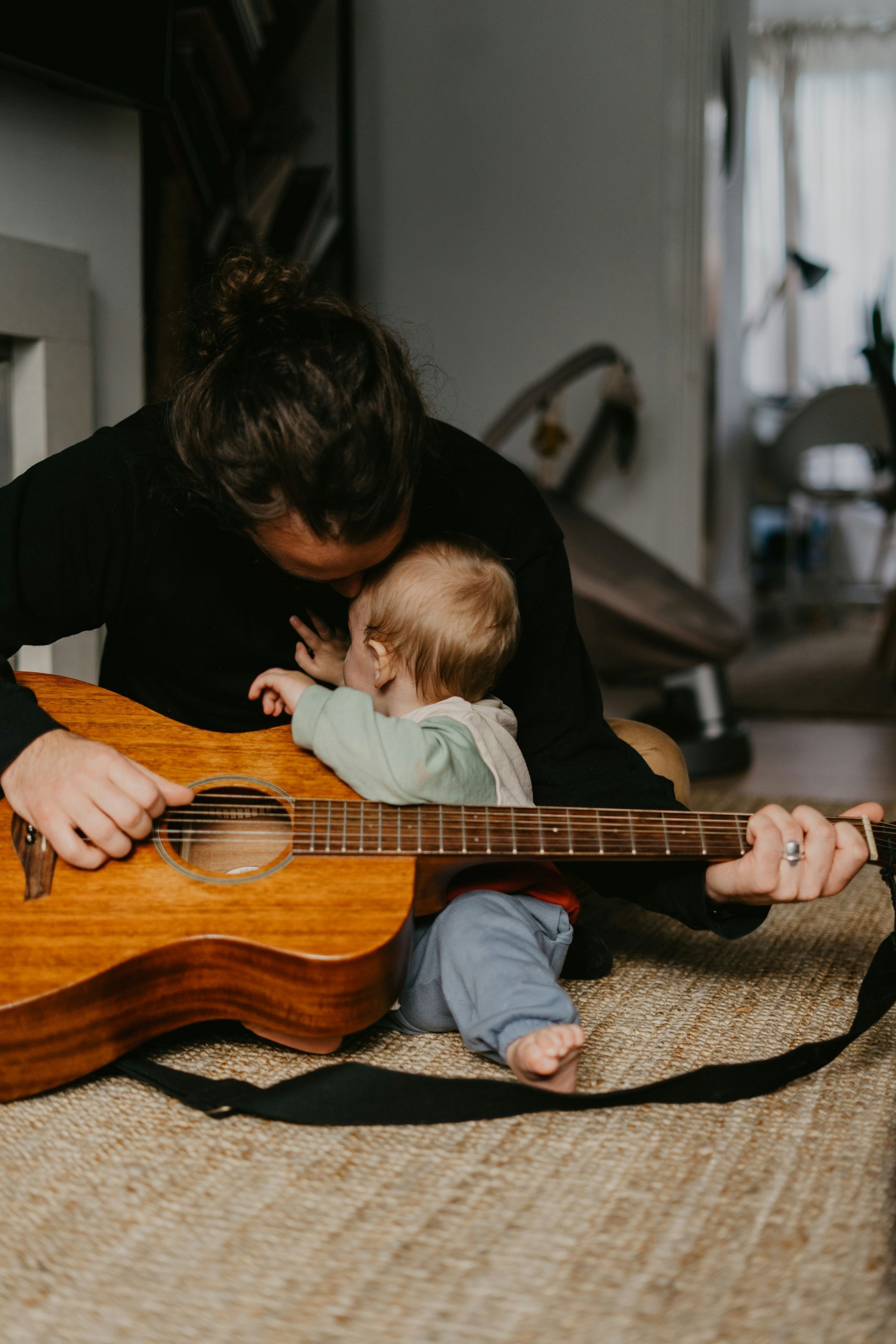 A man is playing a guitar while holding a baby.