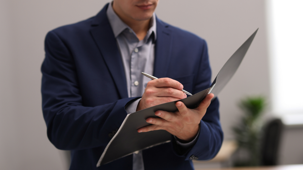 Person in blue suit writing in a black folder, indoor setting.