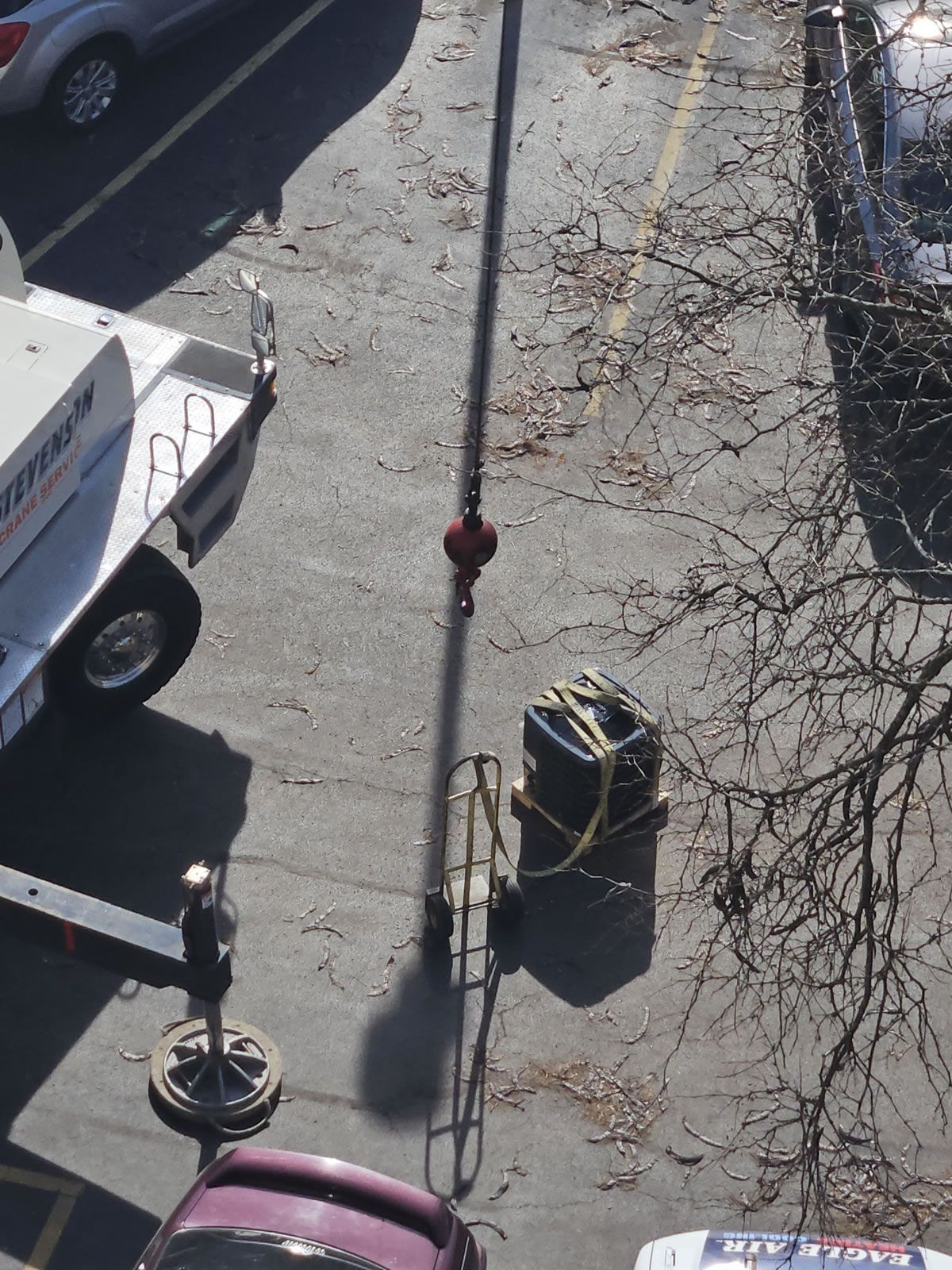 Overhead shot of a tall crane with a load, in a parking lot near trees and vehicles.
