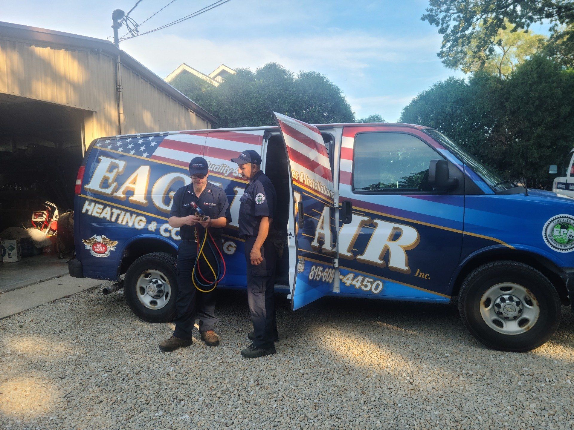 Two HVAC technicians standing near their van. Van is blue, with a flag design.