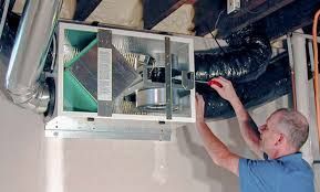 A person installing an air handler in a basement, using a screwdriver.