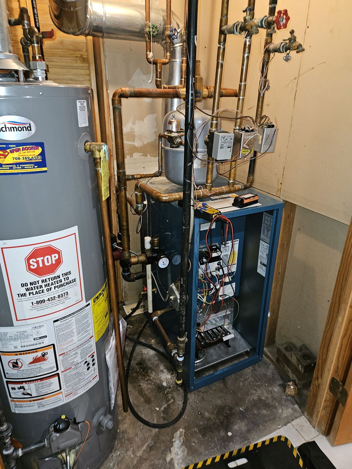 Furnace and water heater in a basement. Blue furnace cabinet with electrical components; silver water heater to the left.