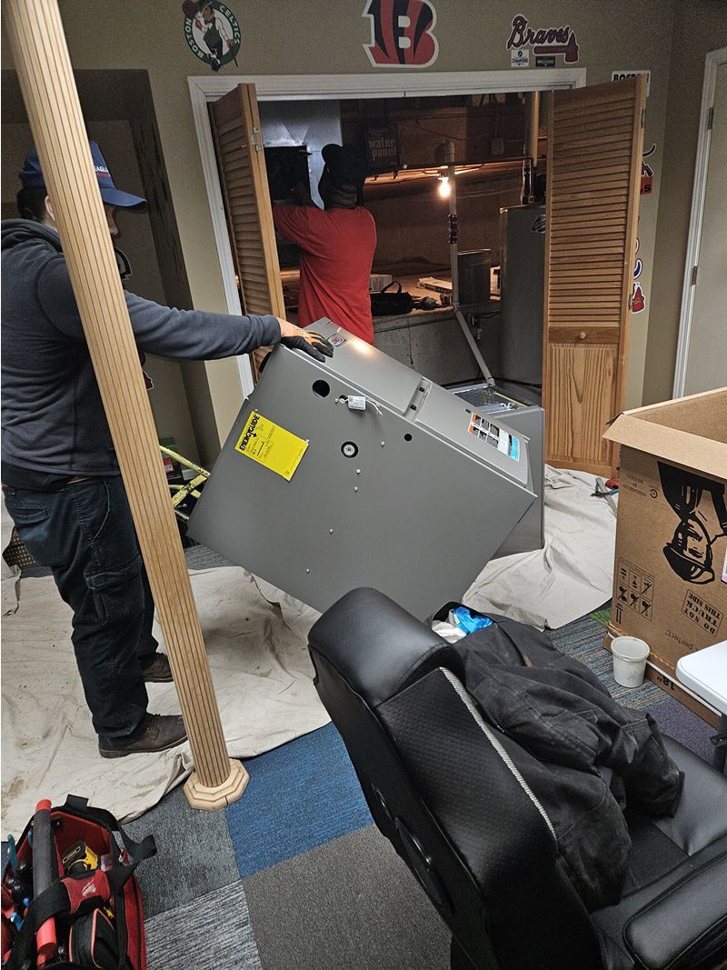 Two people removing an HVAC unit from a doorway. The unit is silver. Setting is indoors.